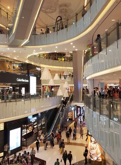 people are walking around in an indoor shopping mall with escalators and balconies