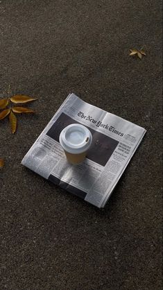 a coffee cup sitting on top of a newspaper next to some leaves and fallen leaves