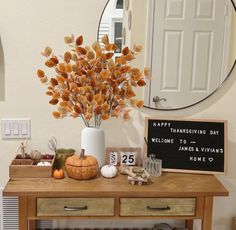 a wooden table topped with a white vase filled with orange flowers next to a mirror