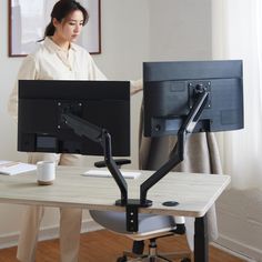 a woman standing in front of two computer monitors on a desk with a cup of coffee next to her