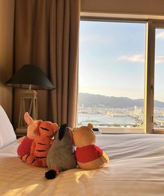 two stuffed animals sitting on top of a bed in front of a window with a city view