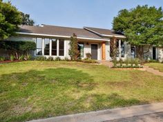 a house that is sitting in the grass with trees and bushes on either side of it