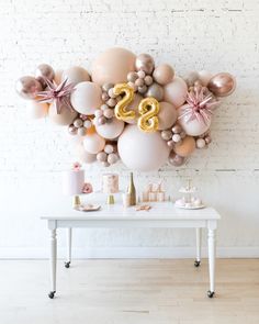 a table topped with balloons and numbers on top of a white wall next to a brick wall