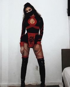 a woman in black and red outfit standing next to a white wall with her hands on her hips