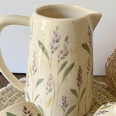 a white pitcher with purple flowers painted on it next to two small plates and a basket