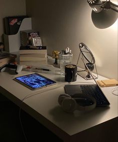 a laptop computer sitting on top of a desk next to headphones and a lamp