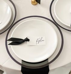 the table is set with white plates and black napkins, gold place cards and silverware