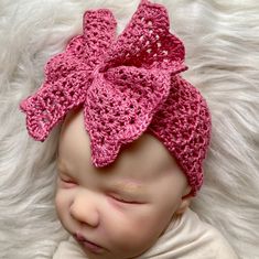 a newborn baby wearing a pink crocheted bow headband on top of a white blanket