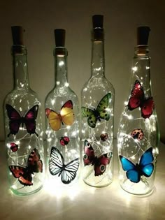 three empty bottles with butterflies on them and some lights in the bottom one is lit up