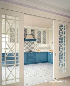 an open kitchen with blue cabinets and white tile flooring on the walls is seen through glass doors