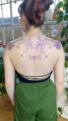 a woman with tattoos on her back standing in front of a potted plant and window