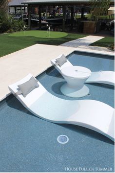 an outdoor swimming pool with white furniture and grass