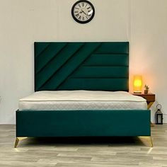 a bed with a green upholstered headboard and foot board next to a clock on the wall