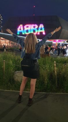 a woman standing in front of a building at night with her arms up and hands raised