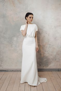 a woman in a white dress standing on a wooden floor with her hand to her ear