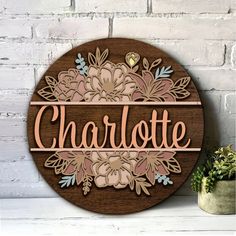 a wooden sign that says charlotte with flowers and leaves in the center on a white brick wall