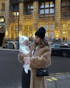 a woman holding a baby in front of a large building with christmas lights on it