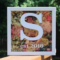 the letter s is surrounded by flowers in front of a wooden bench with trees behind it