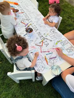 three children sitting at a table drawing with markers and crayons on the paper