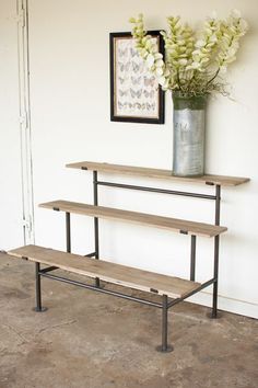 a metal vase with flowers on top of a wooden shelf next to a wall mounted art piece