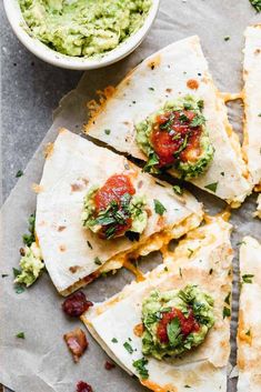 several quesadillas with guacamole and salsa on top, next to a bowl of guacamole