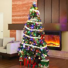 a decorated christmas tree with lights and presents in front of a fire place on the floor