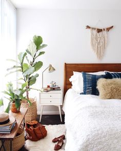 a bedroom with a bed, nightstand and plants on the side table in front of it