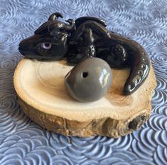 a black frog figurine sitting on top of a piece of wood with a ball in it's mouth