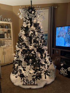 a black and white christmas tree decorated with clear ribbon, bows and ornaments in front of a tv