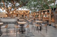 an outdoor restaurant with tables and stools under the tree's branches, next to a bar