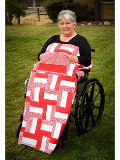 a woman in a wheel chair holding up a red and white quilt on the grass