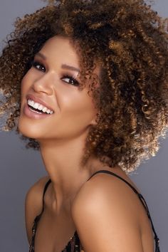 a woman with curly hair smiling and wearing a black dress on top of a gray background