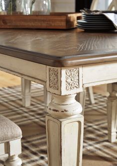 a dining room table with chairs and plates on top of it, in front of a plaid area rug