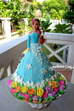 a cake shaped like a woman in a blue dress with flowers on the bottom and sides