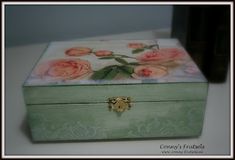 a green box with pink roses painted on the lid and gold handles is sitting on a white table