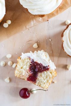 cupcakes with white frosting and cherries sitting on top of a wooden table