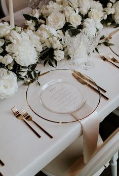 the table is set with white flowers and gold place settings