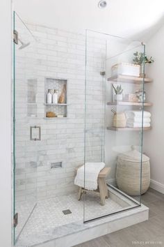 a walk in shower with glass doors and shelves on the wall, along with a stool