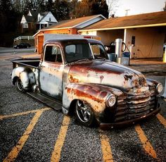 an old rusted truck parked in a parking lot next to a gas station and building