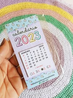 someone holding a calendar in their hand on a crocheted rug with rainbows