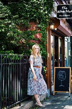 a woman is standing on the sidewalk in front of a wine shop wearing a dress