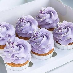 six cupcakes with purple frosting in a white box