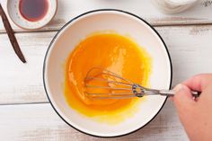 a person whisking orange liquid in a white bowl on top of a wooden table