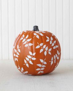 an orange pumpkin with white leaves painted on it's side sitting in front of a white wall