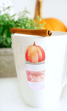 a cup with a sticker on it sitting next to a potted plant and some pumpkins