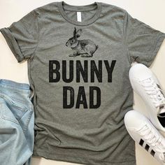 Bunny Dad short-sleeve crewneck t-shirt. Unisex Fit. Printed with eco-friendly water-based inks. Please refer to the size chart in the last image of the listing (laying flat measurements in inches). Due to the calibration differences between computer monitors, phone screens and tablets, the actual product color may vary slightly from what you are viewing.SHIRT FEATURES:- 4.2 oz., Solid color tees (red, white, blue, green) are 100% combed and ringspun cotton, 30 singles- Athletic Heather Shirt (l Gray Crew Neck T-shirt With Funny Print, Casual Tops With Funny Print For Father's Day, Casual Short Sleeve Tops For Father's Day, Father's Day T-shirt With Funny Print In Relaxed Fit, Father's Day Crew Neck Top With Funny Print, Casual Father's Day Shirt With Screen Print, Casual Screen Print Shirt For Father's Day, Father's Day Funny Print Crew Neck Top, Father's Day Funny Print Short Sleeve T-shirt