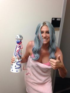 a woman in a towel holding a vase and giving the thumbs up while standing next to a wall