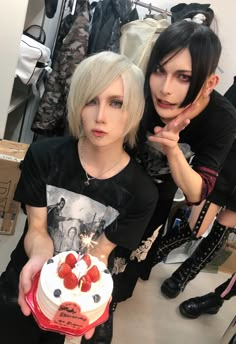 two women with short hair holding a cake in front of their face and looking at the camera