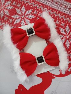 two red and white bows with black stones on them sitting on a piece of fabric