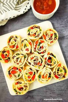 an assortment of vegetable wraps on a cutting board next to a bowl of tomato soup